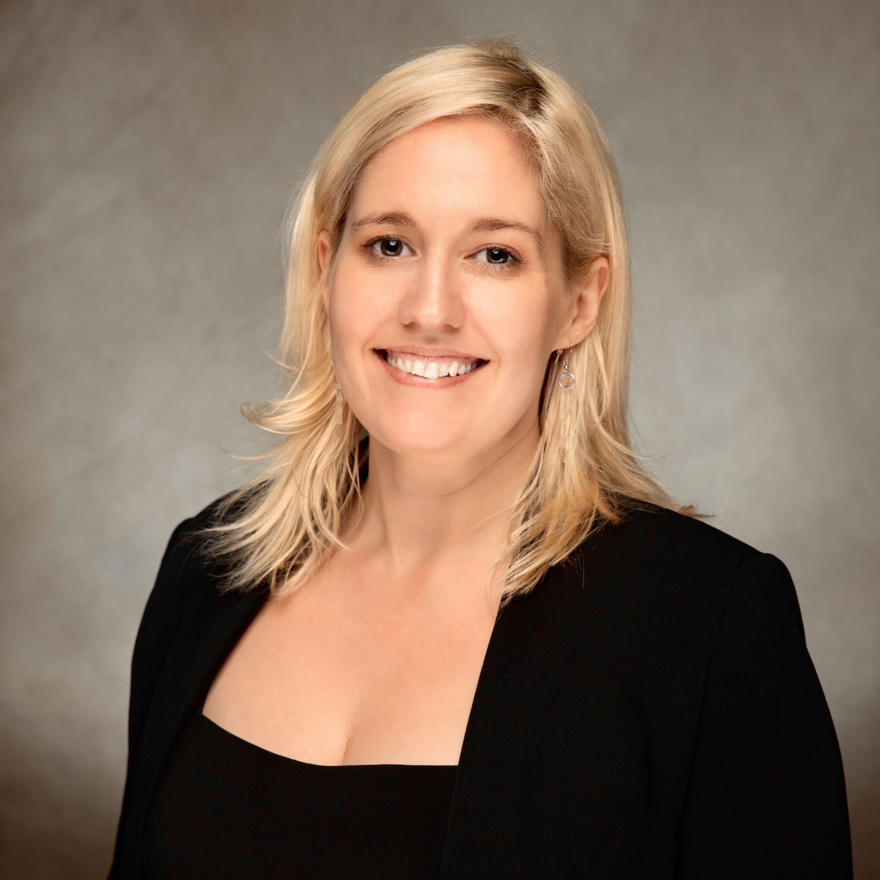 Simonette Berry headshot. She is in a dark suit in front of a dark grey background. 